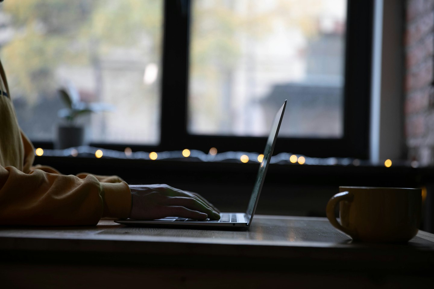 Hands typing on a laptop next to a yellow mug.